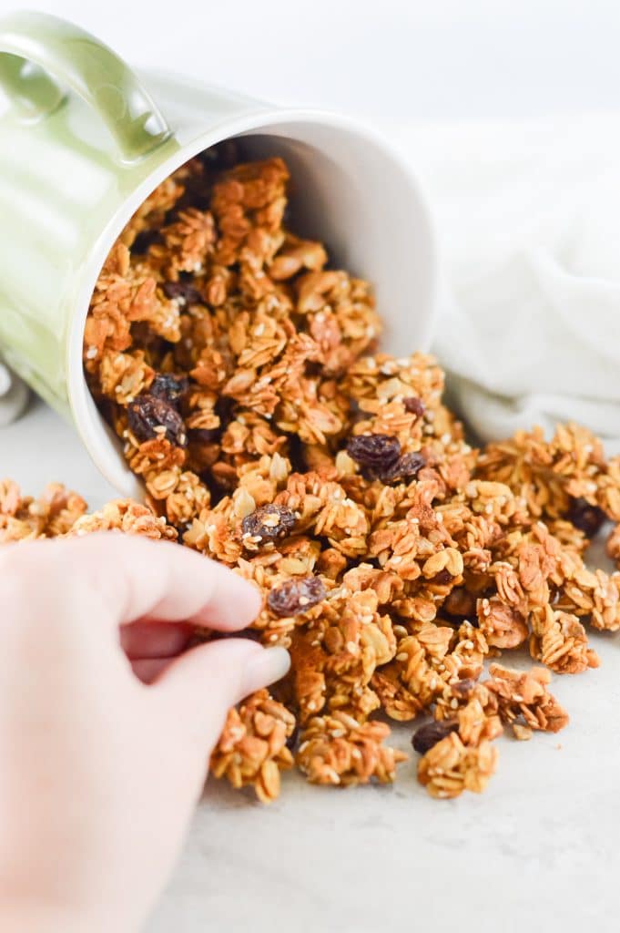a hand lifting a cluster of pumpkin granola from a container
