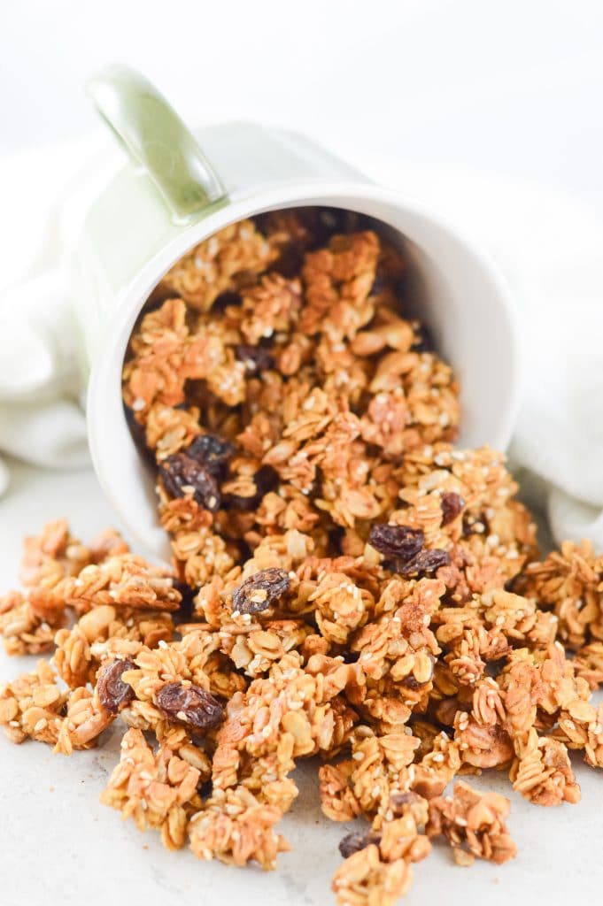 Pumpkin spice granola spilling out of a cup onto a white background