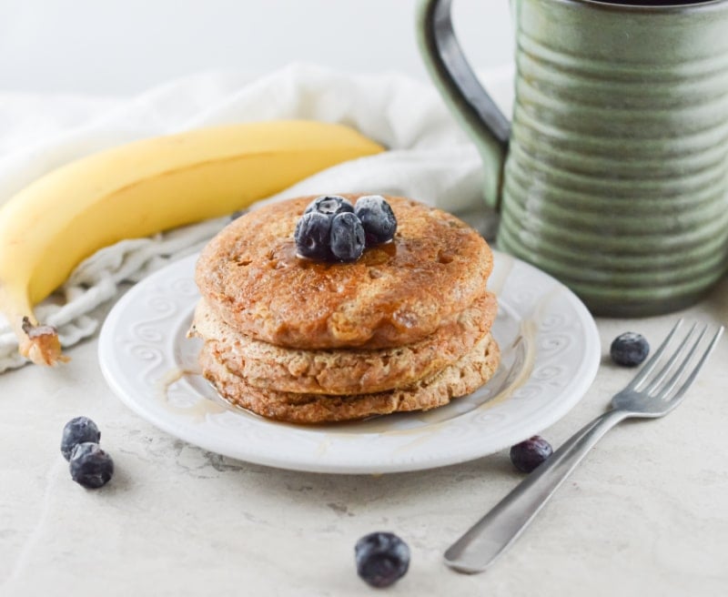 vegan whole wheat pancakes on a white plate with a green mug in the background