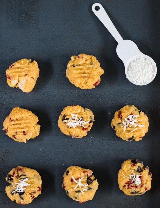 Raw coconut flour cookies on a baking sheet with a spoonful of coconut on the side