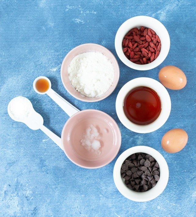 Ingredients for coconut flour cookies laid out in small white bowls against a blue background