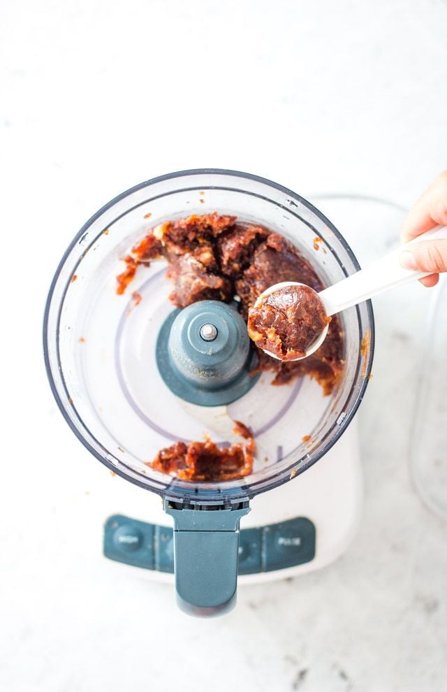 A teaspoon removing some date caramel from the bowl of the food processor.