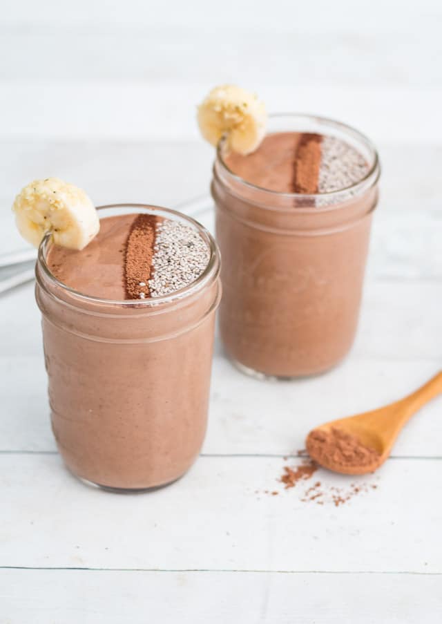 Chocolate smoothie in a mason jar with chia seeds and a banana slice on top, set against a white background