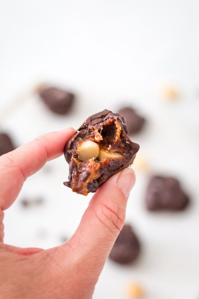 A hand holding up a chocolate covered macadamia cluster that has been bitten
