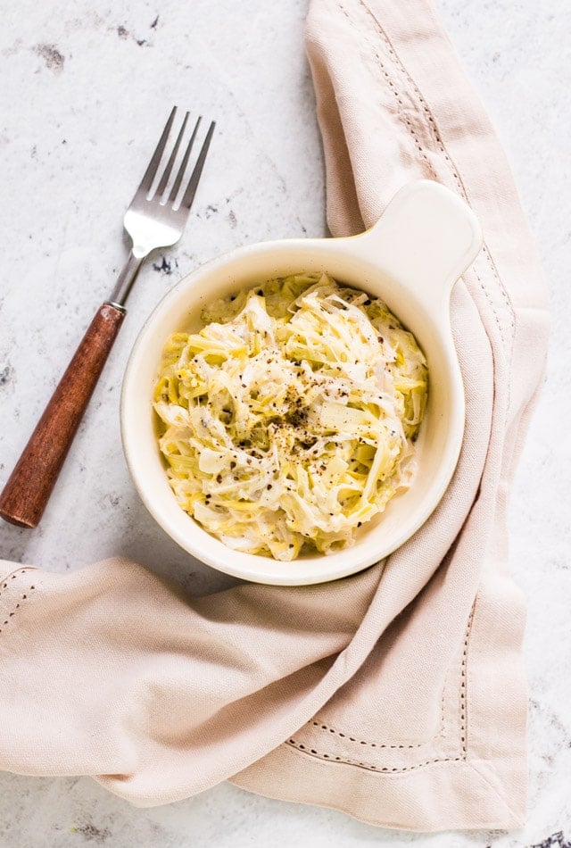 Creamed leeks with creme fraiche sprinkled with lots of black pepper and served in a green and cream bowl with linen surrounding it