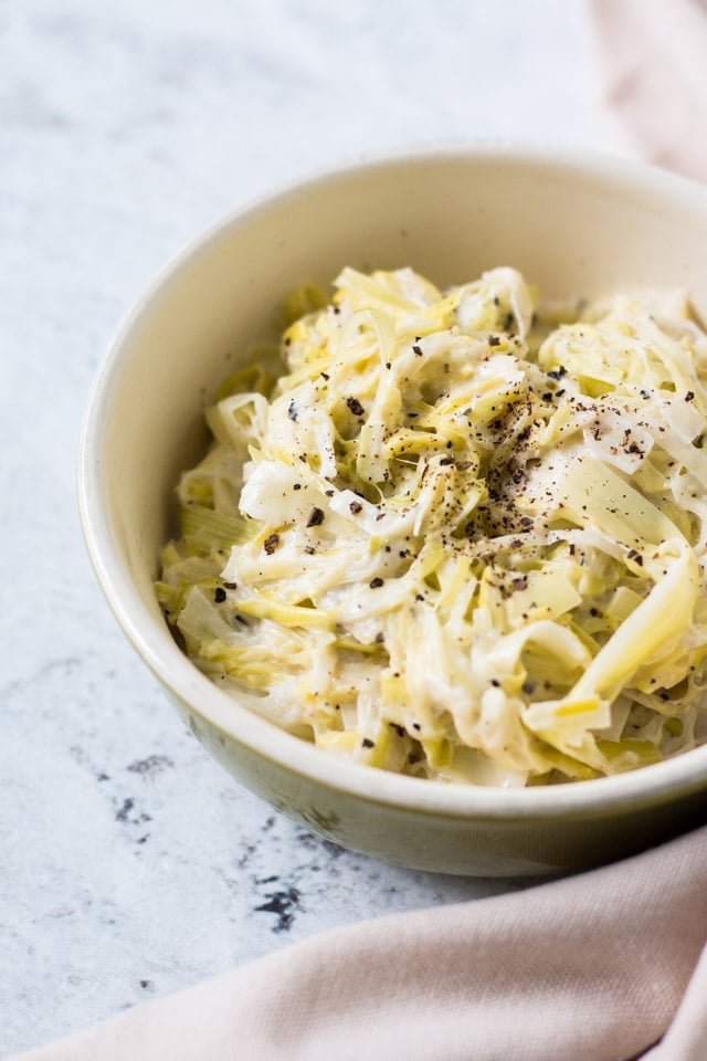 Creamed leeks with creme fraiche sprinkled with lots of black pepper and served in a green and cream bowl with linen surrounding it