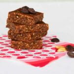 A stack of 4 lara bars on a fun pink and white scrap of fabric with some scattered peanuts and chocolate chips to the side