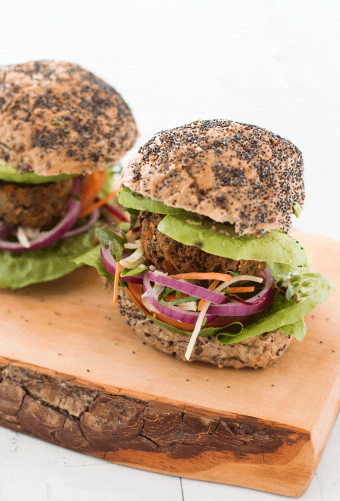 Sweet Potato and Black Bean Burgers in a seeded bun with lettuce, tomato and onions, served on a wooden board