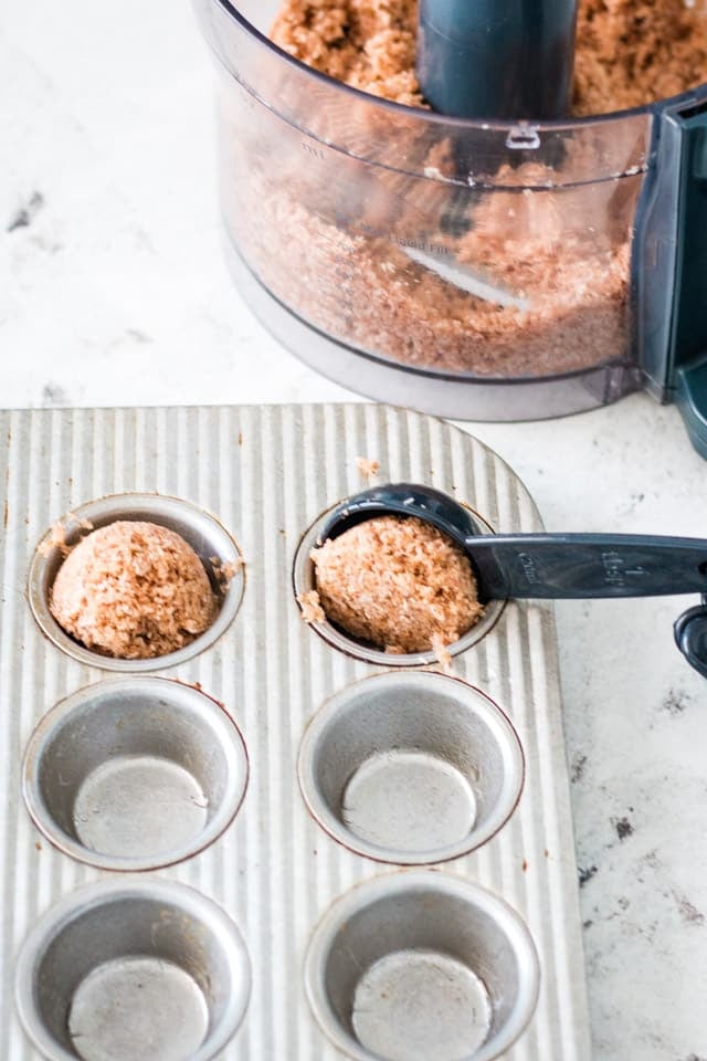 A tablespoon scooping coconut butter bite mixture into a mini muffin tray