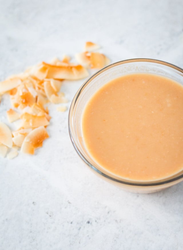 Smooth coconut butter served in a small glass bowl with toasted coconut flakes in the background