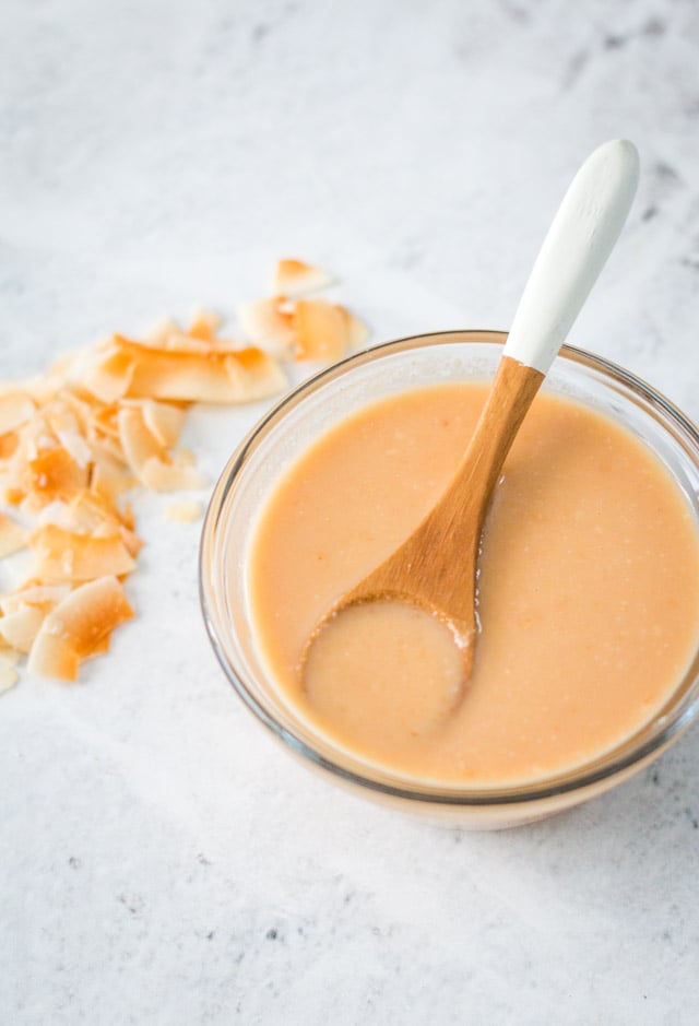 Homemade toasted coconut butter served in a small glass bowl with a wooden and white spooning resting on top