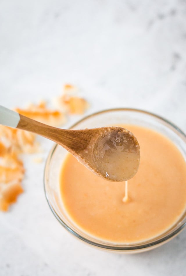 A small white and wooden spoon picking spooning up some coconut butter from a small glass bowl