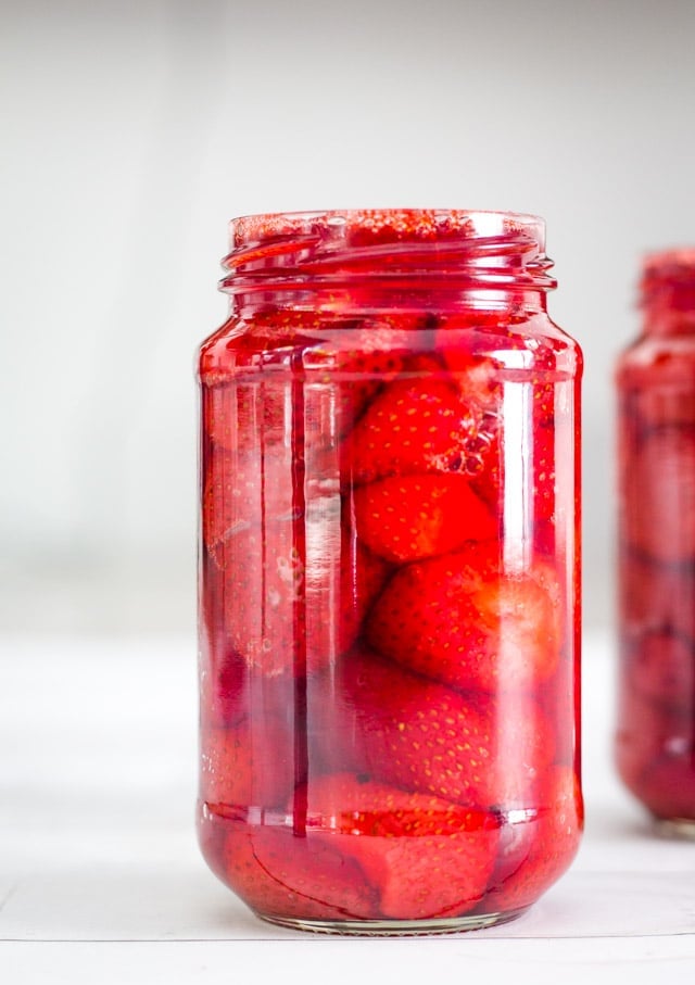 Tall glass jar filled to the brim with baked strawberries and syrup