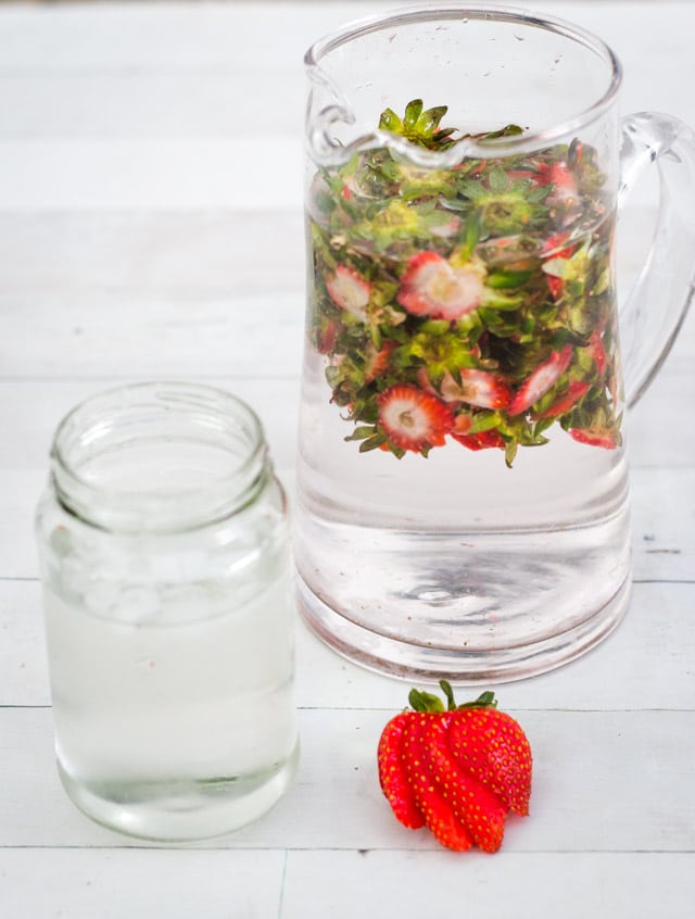 The tops of hulled strawberries gathered in a jug and topped with filtered water to make strawberry infused water