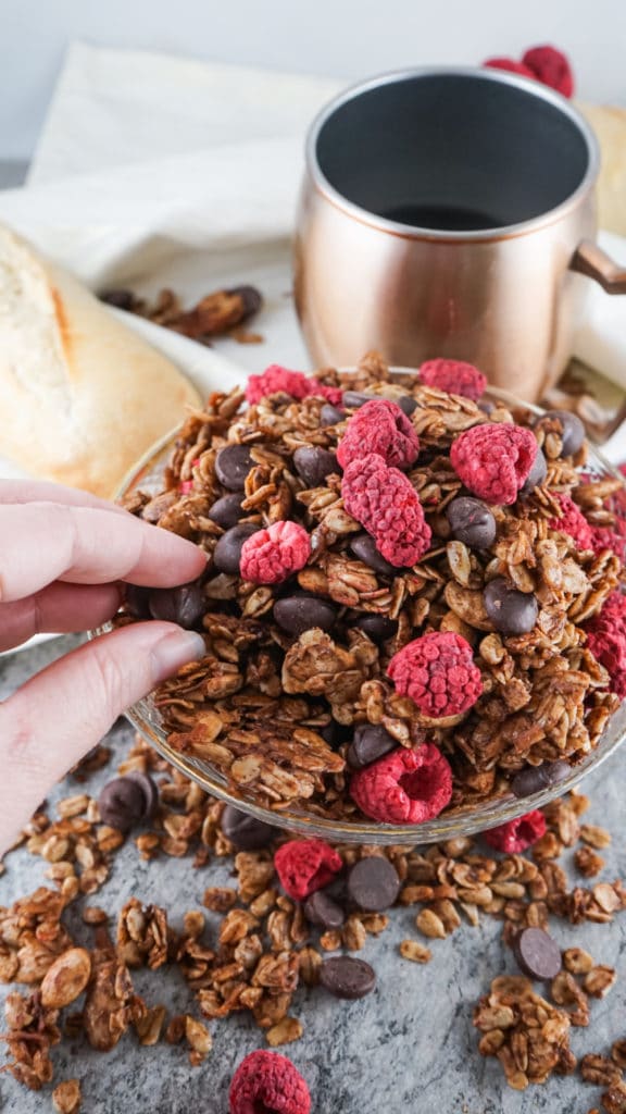 Homemade chocolate granola served in a glass bowl with a cup of coffee in the background