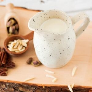 homemade nut milk served in an off white milk jug surrounded by various raw nuts