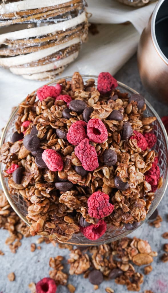 Overhead shot of chocolate granola with lots of raspberries on top and a christmas bauble in the background