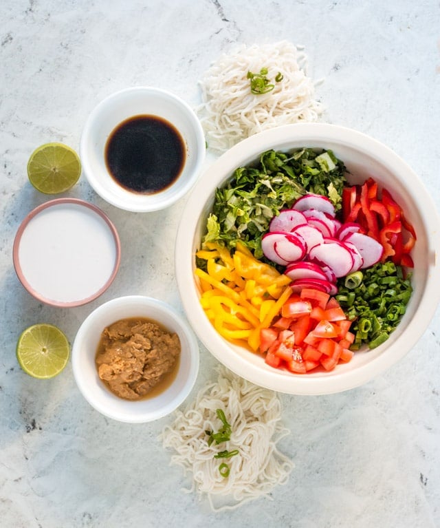 Ingredients for peanut butter noodles displayed in small bowls against a grey background