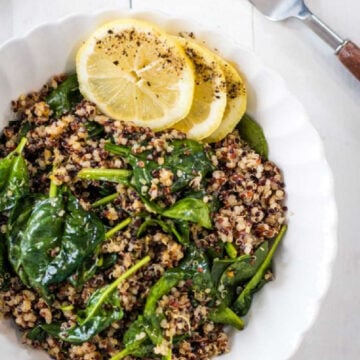 Garlic quinoa and spinach served in a white bowl and topped with lemon slices.