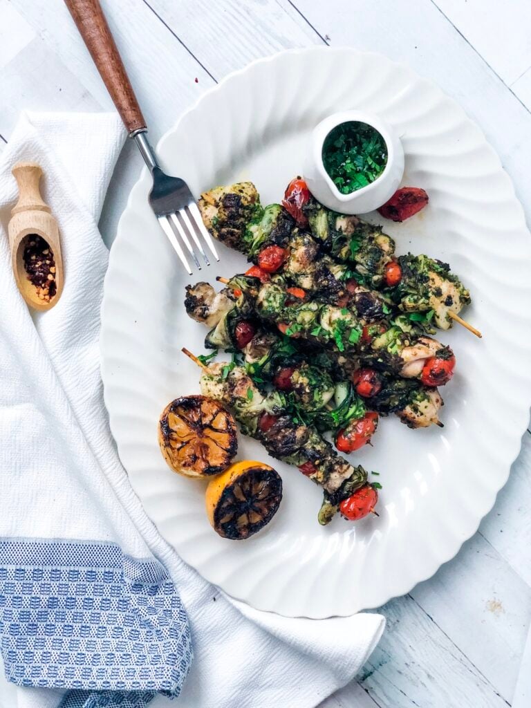 Grilled Chicken Kabobs on a white platter with some salsa verde and grilled lemons