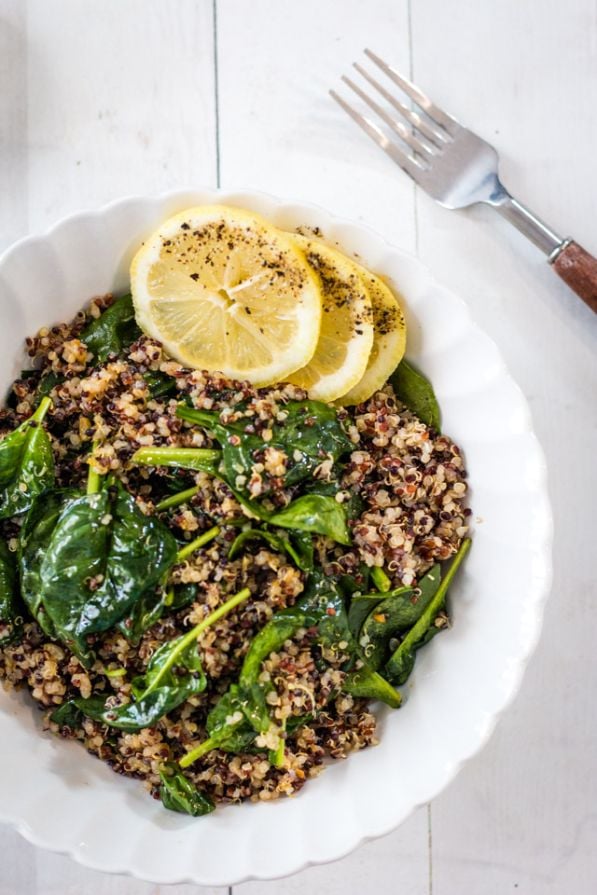 Lemon slices on top of spinach and quinoa served in a white bowl