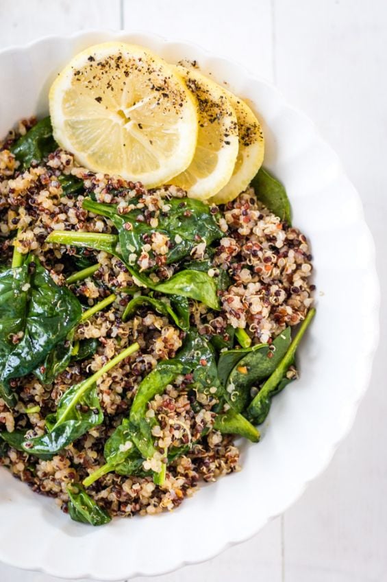 Garlic quinoa and spinach served in a white bowl and topped with lemon slices.