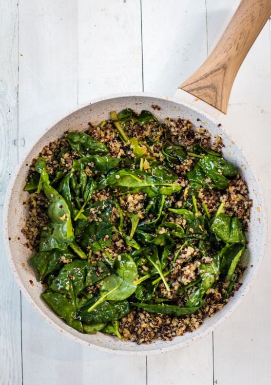 Spinach and lemon zest added to a saucepan of garlic quinoa