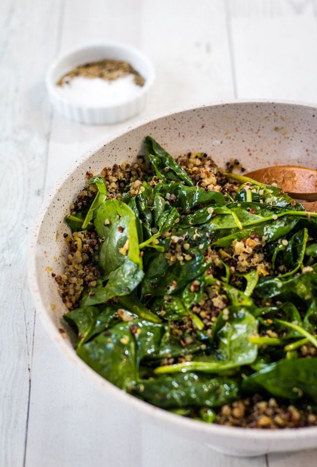 Spinach and quinoa cooking in a medium sized saucepan with a small bowl of salt and pepper in the background