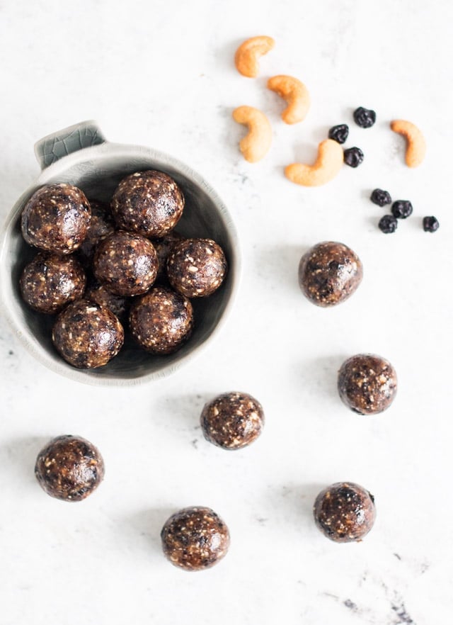 Overhead shot of cashew bliss balls arranged against a white background with a sprinkling of cashews and dried blueberries in the background