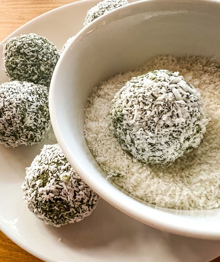 Matcha balls being rolled in a shallow bowl of coconut