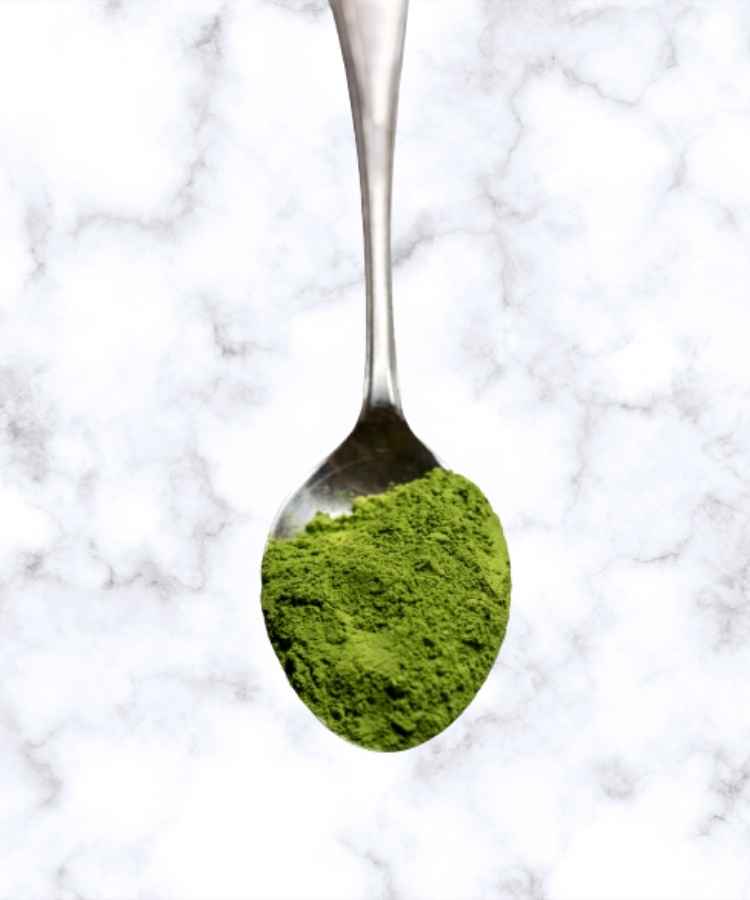 green tea matcha powder on a silver spoon against a marble background