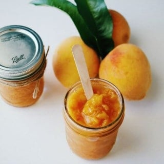 3 Ingredient Peach Butter in mason jars with 3 fresh peaches in the background