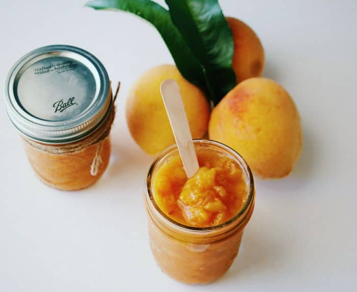 3 Ingredient Peach Butter in mason jars with 3 fresh peaches in the background