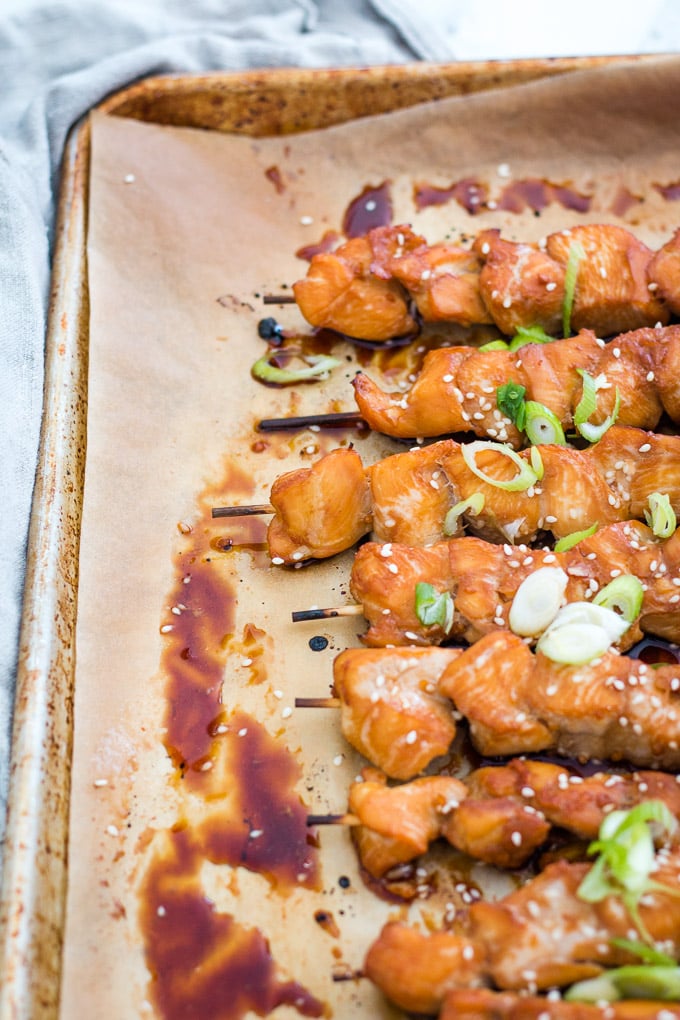 teriyaki chicken skewers on a baking sheet on top of some parchment paper. 