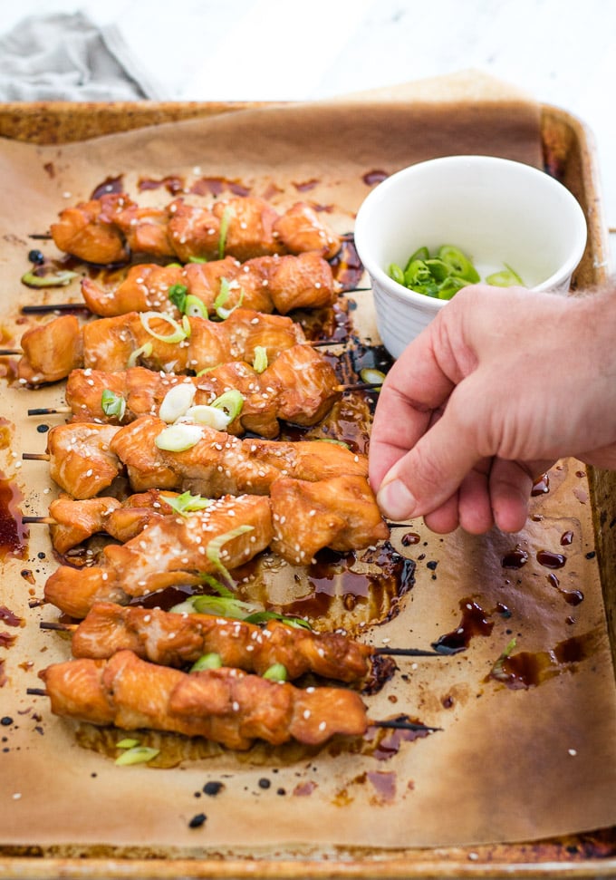 hand lifting a chicken kabob from a baking sheet