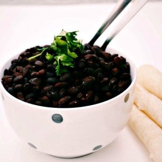 Slow Cooker Savory Black Beans served in a black and white spotted bowl with folded tortillas in the background