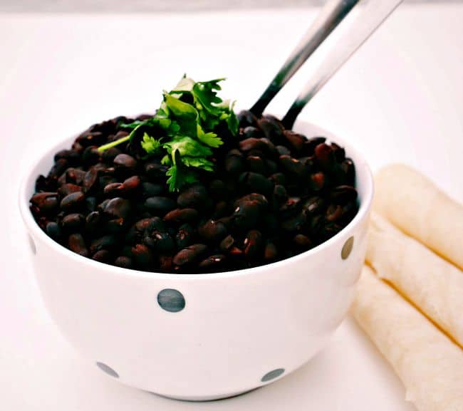 Slow Cooker Savory Black Beans served in a black and white spotted bowl with folded tortillas in the background