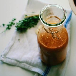 Overhead shot of homemade tomato sauce in a glass jar with some fresh herbs in the background