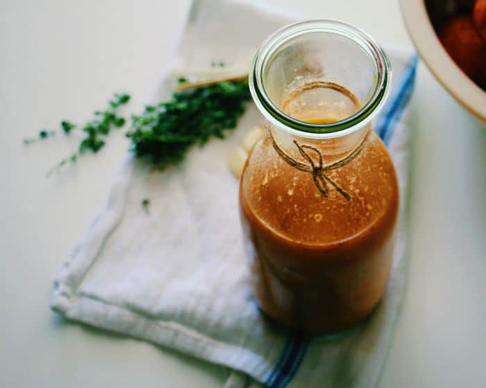 Overhead shot of homemade tomato sauce in a glass jar with some fresh herbs in the background