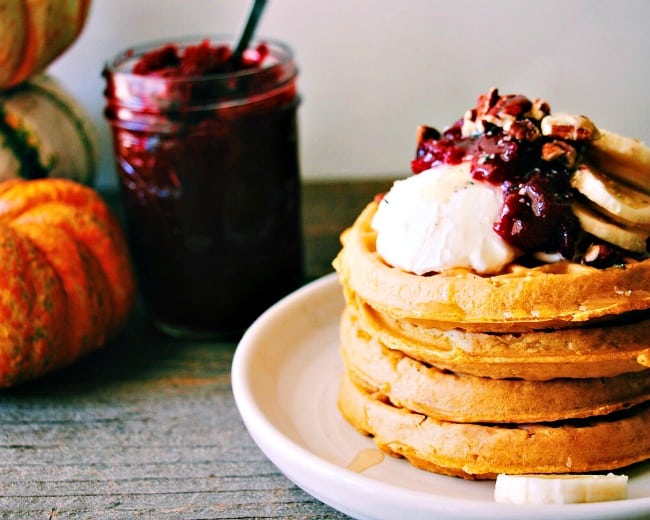 Stack of waffles topped with cranberry butter and yogurt with a glass jar full of cranberry butter in the background