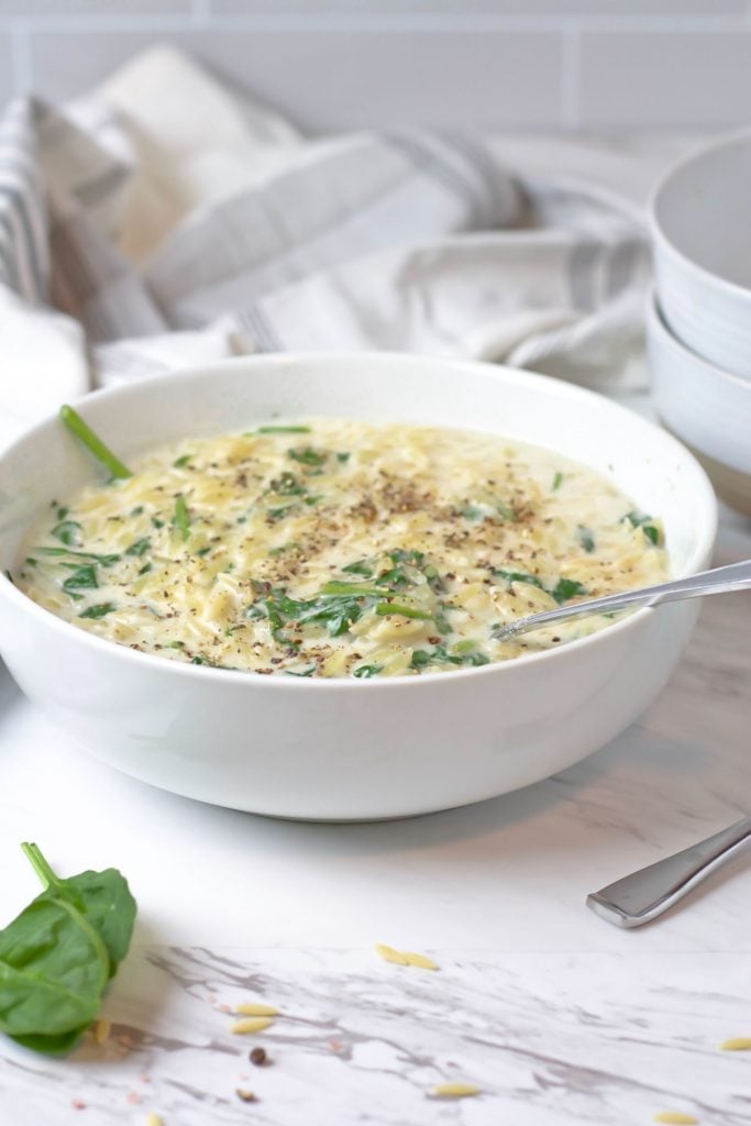 Creamy risoni served in a white bowl with loose spinach and risoni sprinkled around
