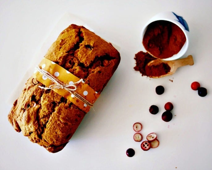 Overhead shot of Whole Wheat Pumpkin Bread with a splattering of fresh cranberries and a little container of pumpkin spice in the corner