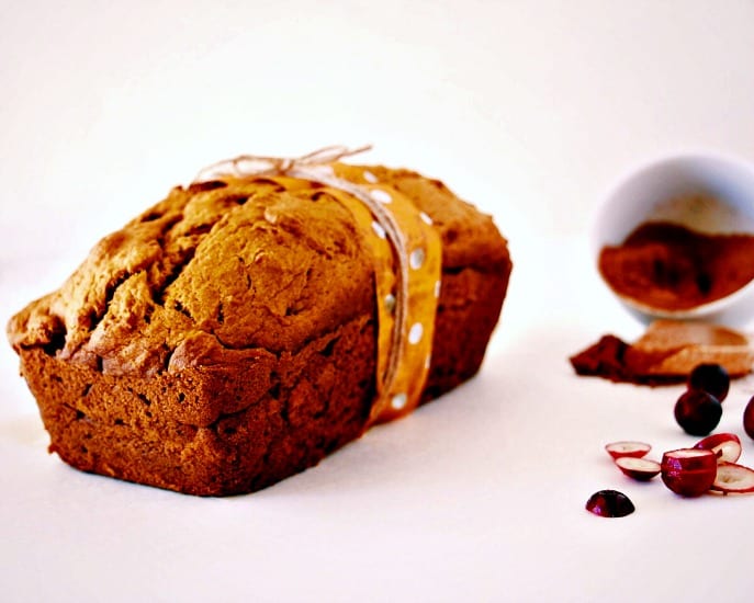 front on shot of Whole Wheat Pumpkin Bread with a splattering of fresh cranberries and a little container of pumpkin spice in the corner