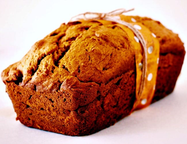 Pumpkin and Fresh Cranberry Bread against a white background. The bread is wrapped in some parchment paper and twine