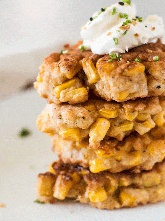 A stack of 4 corn cakes on a beige plate topped with sour cream and spring onions