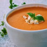 bright orange soup served in a white bowl and topped with fresh herbs