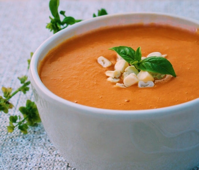 bright orange soup served in a white bowl and topped with fresh herbs