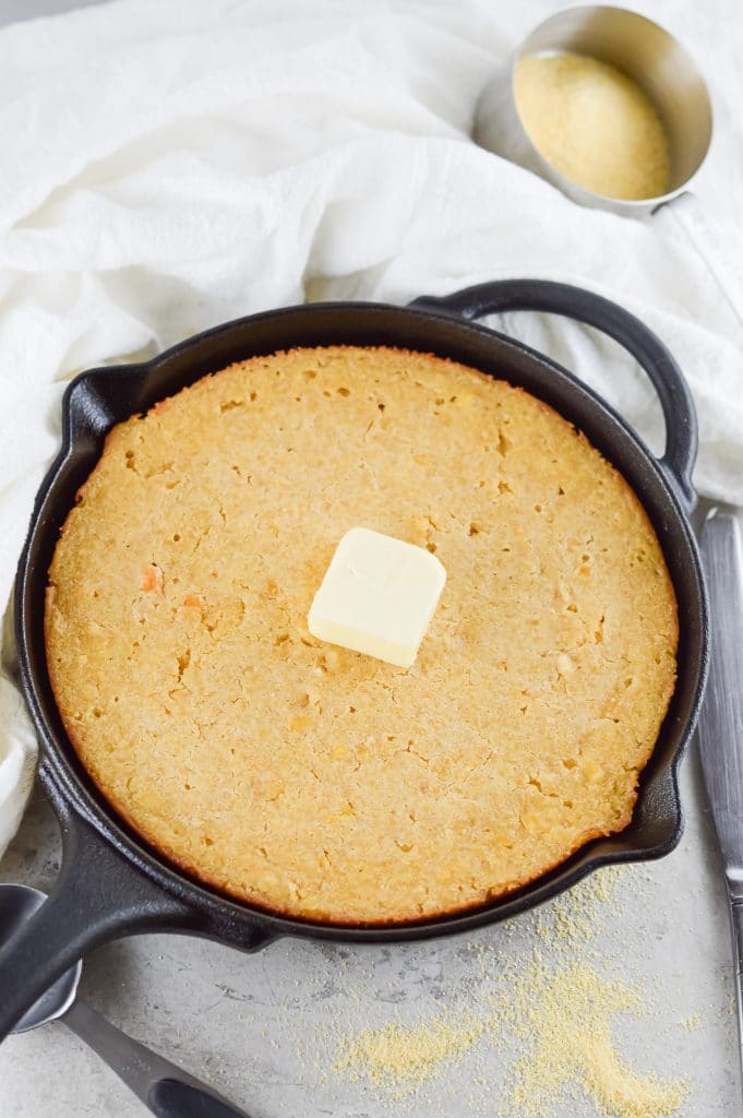 homemade cornbread in a black cast iron skillet with a cube of butter on top