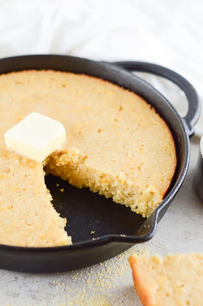 Homemade honey butter cornbread in a cast iron skillet with a dollop of butter on top