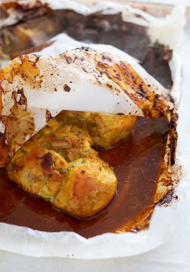 A cooked chicken breast inside a parchment paper package surrounded by turmeric sauce